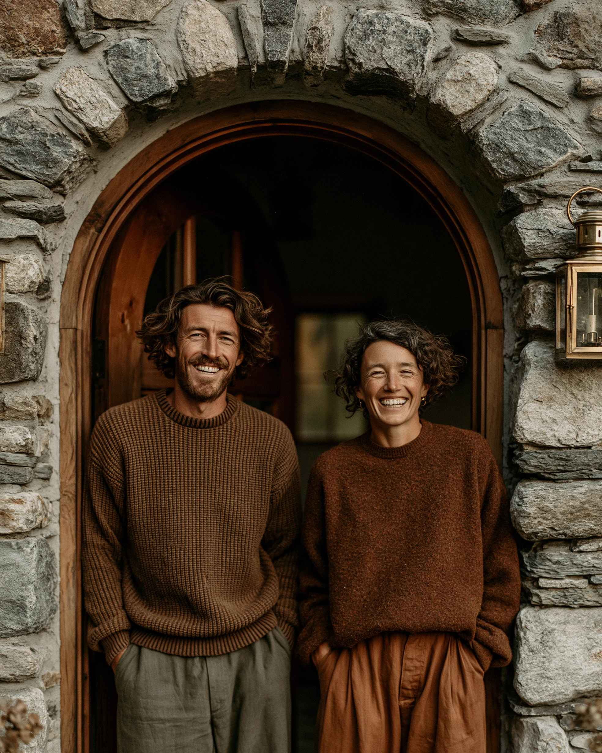 Tom and Eleanor Gresham in the doorway of the inn, candid, warm tungsten light from the bar behind them.